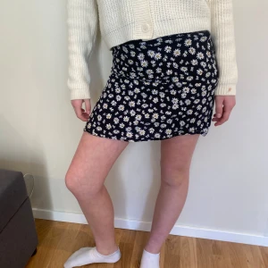 Blommig kortkjol från ONLY - Säljer en söt blommig kortkjol från ONLY i storlek XS. Kjolen har ett svart tyg med vita blommor och en bekväm passform. Perfekt för en somrig look! 🌼Har en dragkedja på sidan och passar perfekt till tröjan min modell har på sig till kjolen i bilden❤️😻🌸