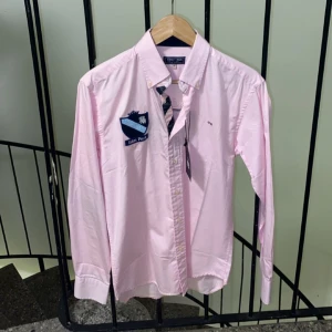 Rosa skjorta från Eden Park - Snygg rosa skjorta från Eden Park med broderade detaljer och nummer 87 på ryggen. Skjortan har långa ärmar och knappar framtill. Perfekt för en stilren look. Äkta 