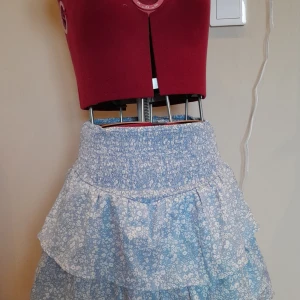 Blommig blå kjol från Gina Tricot - Blå kjol med blommigt mönster från Gina Tricot. Kjolen har en elastisk midja och 2 volanger. 🌸