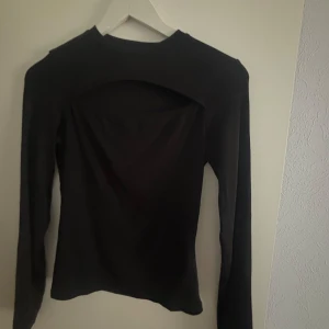 Svart ribbad topp från Amisu - Säljer en svart ribbad topp från Amisu med långärmad design och en unik öppen ryggdetalj. Perfekt för en stilren look. Tillverkad i Turkiet.