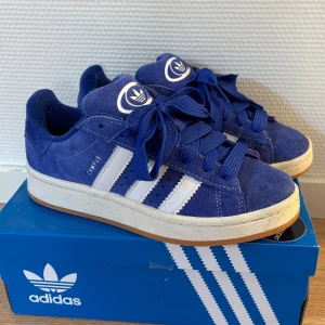 Blå Adidas Campus  - Snygga blå Adidas Campus sneakers, sparsamt använda. Man kan se lite framtill att dem är har används ute (bild 2) men inget man direkt tänker på. Finns även vita skosnören man får med💙