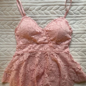 Rosa spetslinne - Säljer ett sött rosa spetslinne med smala axelband och v-ringning. Toppen har en volangdetalj nedtill och är perfekt för somriga dagar. Passar bra till både jeans och kjol 💞