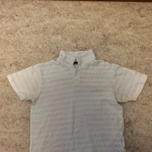 Vit pikétröja från Smog - Säljer en stilren vit pikétröja från Smog i storlek M. Tröjan har ett diskret mönster och korta ärmar, perfekt för en avslappnad look. Tillverkad i ett bekvämt material som passar bra till vardags.