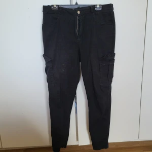 Svarta cargobyxor från BikBok - Säljer ett par svarta cargobyxor från BikBok. Byxorna har flera praktiska fickor och en knappstängning framtill. Perfekta för en avslappnad stil.