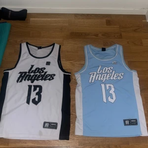 Två basketlinnen från FSBN - Säljer två snygga basketlinnen från FSBN i storlek XS. Ett är vitt med svarta detaljer och texten 'Los Angeles 13', det andra är ljusblått med vita detaljer och samma text. Perfekta för sportiga aktiviteter eller sommarens varma dagar.