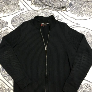 Cardigan från Dressmann - Säljer en stilren svart ribbad cardigan från Dressmann i storlek M. Tröjan har en praktisk dragkedja framtill och är perfekt för både höst och vinter. Den är långärmad och gjord i ett bekvämt material som håller dig varm. Passar både till vardags och lite finare tillfällen. Den är i bra skick med inga defekter eller nått sånt. Säljer eftersom den är för stor för mig.