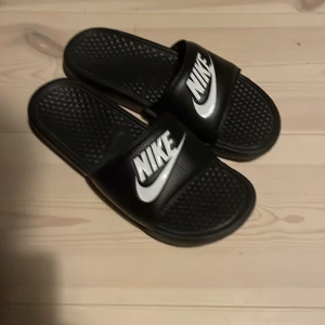 Svarta sandaler från Nike - Säljer ett par svarta Nike sandaler med vit logga. Perfekta för sommardagar med bekväm passform och slitstark sula. Storlek dam 38.