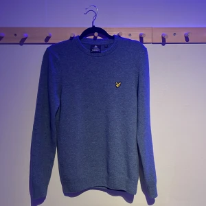 Lyle and Scott knitwear sweater  - Säljer en snygg blå stickad tröja från Lyle & Scott med deras ikoniska gula logga på bröstet. Tröjan har en klassisk rund hals och långa ärmar, perfekt för kyligare dagar. Passar både till jeans och chinos för en stilren look. Passar S och M. 