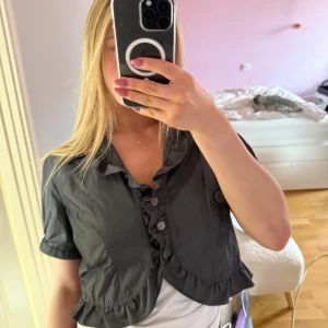 Bolero - Säljer en snygg svart/grå boleromed volangdetaljer och knappar framtill. Perfekt för att ge en stilfull touch till din outfit. 💕