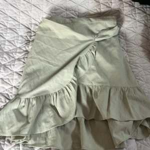 Grön omlottkjol från Vero Moda - Snygg grön omlottkjol från Vero Moda med volangdetaljer. Perfekt för en stilren look. Kjolen har en knytfunktion i midjan för justerbar passform.