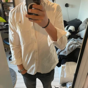 Vit skjorta från Ralph Lauren - Säljer en stilren vit skjorta från Ralph Lauren i slim fit. Skjortan har långa ärmar och klassiska knappar framtill. Den är prydd med det ikoniska broderade Polo-logotypen på bröstet. Perfekt för en elegant look.