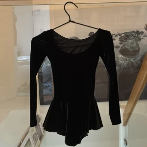 Svart långärmadkonståknings klänning från Mondor - Säljer en elegant svart konståknings klänning i från Mondor med långärmade och en fin kjoldel. Perfekt för olika tillfällen med sin stilrena design. Klänningen har en rund halsringning och är tillverkad i ett mjukt material.