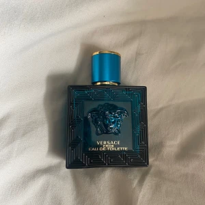 Versace Eros Eau de Toilette  - Säljer en elegant Versace Eros Eau de Toilette i en stilren blå flaska med ett detaljerat mönster och Medusa-motiv. Flaskan har en gyllene kant på korken som ger en lyxig känsla. Perfekt för den som vill ha en doft med karaktär och stil. Ca 15 ml kvar