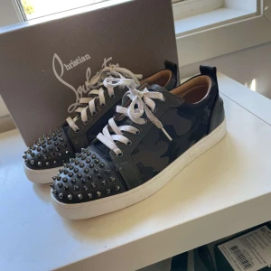 Camo Loubs - Snygga sneakers från Christian Louboutin med ett coolt camouflage-mönster och nitar på tån. Skorna har en klassisk snörning och den ikoniska röda sulan. Perfekta för dig som vill sticka ut!