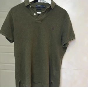 Olivgrön pikétröja från Ralph Lauren - Säljer en olivgrön pikétröja från Ralph Lauren. Tröjan har korta ärmar och en klassisk krage med knappar. Perfekt för en stilren och avslappnad look.