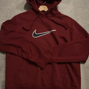 Vinröd hoodie från Nike - Säljer en snygg vinröd hoodie från Nike med klassisk logga på bröstet. Tröjan har en bekväm passform med långa ärmar och en praktisk huva med dragsko. Perfekt för en avslappnad stil.