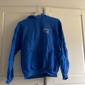 Blå hoodie med tryck - Säljer en blå hoodie med texten 'BÅGE IN' tryckt på framsidan. Tröjan har en praktisk ficka framtill och en luva med dragsko. På ärmen finns en röd patch med texten 'Active Life foundation’.