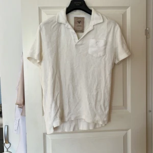 Vit frotté t-shirt från OAS - Säljer en vit frotté t-shirt från OAS, perfekt för att använda direkt efter bad. T-shirten har en liten bröstficka med en broderad palm och korta ärmar. Designad i Sverige och tillverkad i Portugal.