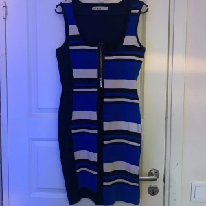Blå och vit randig klänning från Karen Millen - Snygg blå och vit randig klänning från Karen Millen med dragkedja framtill. Klänningen är kortarmad och har en figurnära passform som framhäver silhuetten.  Den är väldigt stretchy ( man kan ha som S till M) Perfekt för en stilren look!