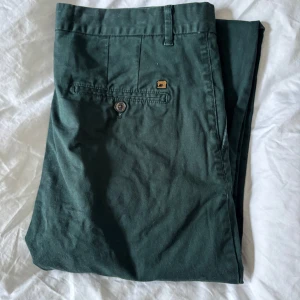 Gröna chinos från Scotch & Soda - Snygga gröna chinos från Scotch & Soda. Byxorna har en slimfit passform med knappar bak och en stilren design. Perfekta för en avslappnad men ändå uppklädd look.