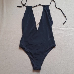 Svart baddräkt med knytband - Snygg svart baddräkt med djup v-ringning och knytband i nacken. Djupt ringad I ryggen. Tillverkad i ett mjukt och bekvämt material som ger en smickrande passform. Kan knytas på olika sätt. Endast testad (med underkläder under såklart) 