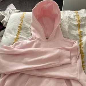 Ljusrosa hoodie - Säljer en ljusrosa hoodie med en stor ficka framtill och en mysig huva. Perfekt för en avslappnad stil. Den har långa ärmar och ribbade muddar vid ärmslut och nederkant.
