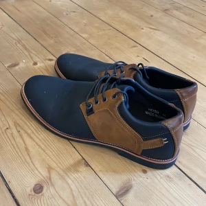 Svart och bruna skor  - Snygga skor från Tuop i svart och brunt med snörning. Skorna har en rund tå och en stilren design som passar perfekt för olika tillfällen. Tillverkade i syntetmaterial med en slitstark sula.