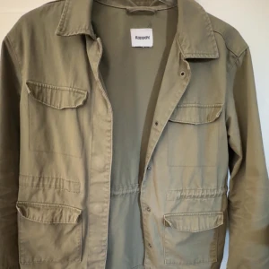 Beige jacka från Kappahl - Snygg grön vår/sommar jacka från Kappahl med flera fickor, knappar framtill och resår i midjan. 