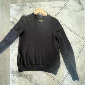 Svart tröja från BOSS - Säljer en stilren svart tröja från BOSS, tillverkad av finaste italienska garn. Tröjan har en klassisk design med rund hals och långa ärmar, perfekt för en elegant look.