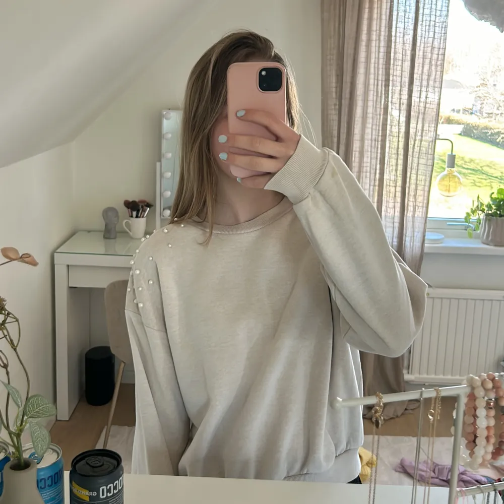 Säljer en stilren beige tröja med pärldetaljer på axlarna. Tröjan har långa ärmar och en bekväm passform, perfekt för en avslappnad look. Den är gjord i ett mjukt material som känns skönt mot huden.. Neuletakit & Villapaidat.