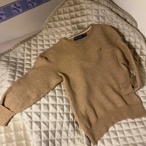 Beige 3/4-ärmad tröja från Polo Ralph Lauren - Säljer en stilren beige trekvartsärmad tröja från Polo Ralph Lauren. Tröjan har en broderad logotyp på bröstet och är tillverkad i ett mjukt material. Perfekt för en klassisk och avslappnad look.