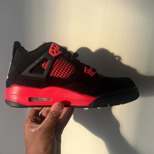 Svarta och röda sneakers från Nike - Snygga svarta och röda air Jordan 4med ikonisk design. Skorna har en svart bas med röda detaljer och en vit logga på hälen. Perfekta för dig som vill ha en stilren och sportig look.använts en gång!!! Ingen original förpackning 