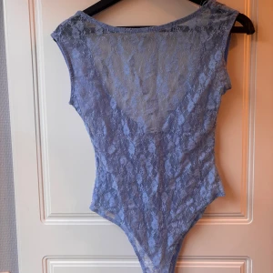 Ljusblå spetsbody - Säljer en ljusblå body i spets med djup rygg. Toppen är figursydd, Perfekt att styla med jeans eller kjol för en trendig look.