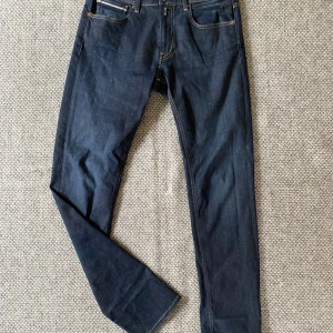 Mörkblå jeans Replay Grover herr - Säljer ett par mörkblå jeans från Replay, modell Grover. Klassisk femficksdesign med snygga kontrastsömmar och diskret Replay-logga vid fickan. Jeansen har rak passform och är tillverkade i slitstarkt denimtyg.