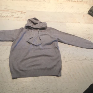 Grå merino hoodie - Säljer en enkel grå merino hoodie med huva och dragsnören. Tröjan har långa ärmar och ribbade muddar vid ärmslut och nederkant. Perfekt för en avslappnad stil.