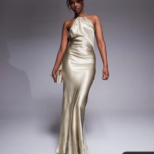 Champagnefärgad långklänning i satin med öppen rygg - Säljer en elegant champagnefärgad långklänning i glansig satin. Klänningen har halterneck med knyt i nacken och en snygg öppen rygg. Perfekt som balklänning!! Helt ny med prislapp kvar, helt slutsåld!