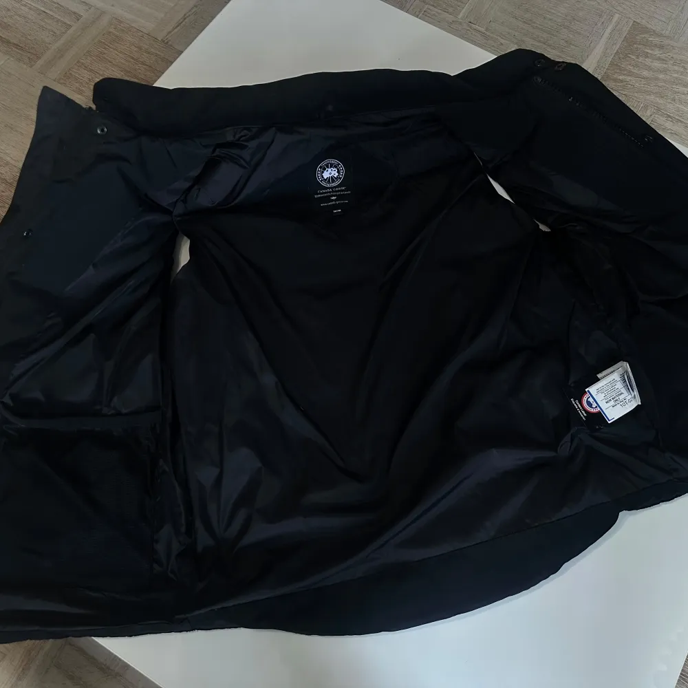 Säljer en stilren svart dunväst från Canada Goose med knappar framtill och två praktiska fickor. Västen har en broderad logotyp på bröstet och är perfekt för kyligare dagar. Passar både till vardags och mer avslappnade tillfällen.. Takit.