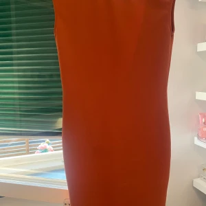 Rostfärgad ärmlös klänning med v-ringning - Säljer en snygg rostfärgad klänning med djup v-ringning fram. Klänningen är ärmlös och har en rak, enkel siluett som ger en stilren look. Perfekt för dig som gillar minimalistisk stil.