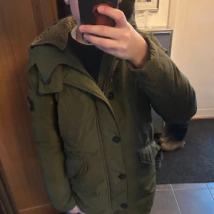 Grön dunjacka från Stone Island Junior - Säljer en grön dunjacka från Stone Island Junior med huva och mysigt foder. Jackan har flera fetures som fickor, knappar och knappar till luvan. !Kom med prisförslag!