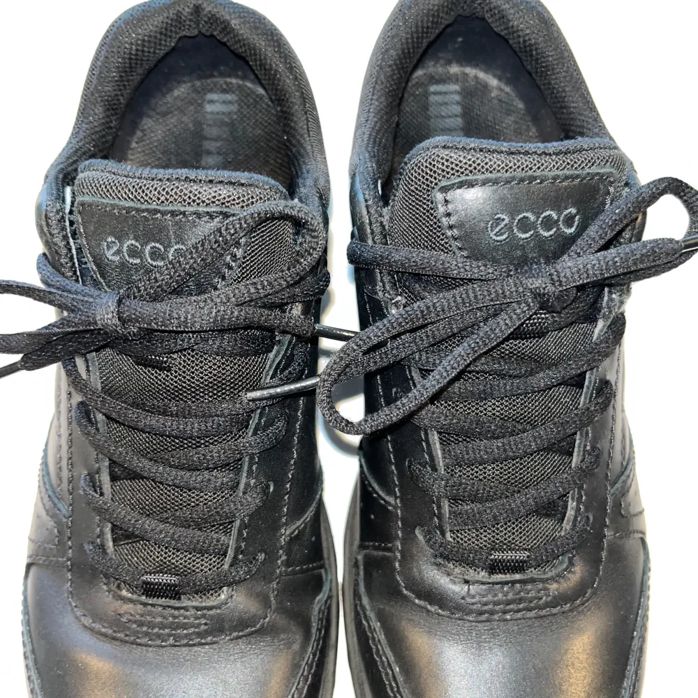 Snygga svarta sneakers från Ecco med snörning och Gore-Tex-material för extra skydd mot väta. Skorna har en robust sula med röd detalj för bra grepp och komfort. Perfekta för vardagsbruk och håller dina fötter torra och bekväma.. Kengät.