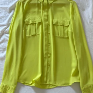 Gul blus från Antea - Snygg gul blus från Antea med långa ärmar och knappar framtill. Blusen har två bröstfickor med lock och en klassisk krage. Perfekt för att lysa upp garderoben! Använd ca 2 gånger. Skriv vid intresse och frågor!