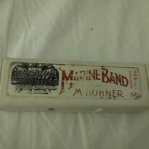 Marine Band munspel från M. Hohner - Säljer ett klassiskt Marine Band munspel från M. Hohner i originalförpackning. Munspelet har en silverfärgad metallkropp och ligger i ett vitt plastetui med tryckt logga och text. Perfekt för dig som gillar musik och vill ha ett ikoniskt munspel.
