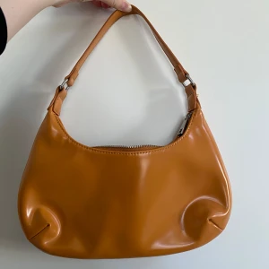 Orange axelväska  - Säljer en snygg brun axelväska i glansigt material. Perfekt för att bära med små nödvändigheter!❤️