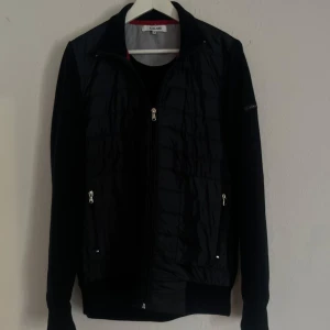 CARDIGAN JACKA - Säljer en stilren eftertraktad mörkblå jacka från Iceland i storlek M. Jackan har en quiltad design med dragkedja framtill och långa ärmar. Tillverkad av 70% bomull och 30% polyester, vilket gör den både bekväm och hållbar. Passar dig som är 180+ ! Passa på inför våren :)