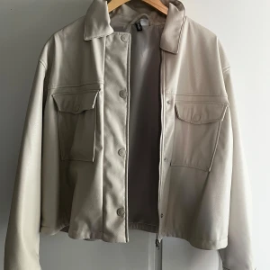 Beige skinnjacka med dragkedja - Snygg beige skinnjacka med dragkedja och knappar framtill. Jackan har två stora fickor med lock på bröstet och en klassisk krage. Perfekt för en stilren look. Säljer denna eftersom den tyvärr blivit för liten, den är dock använd några gånger bara passa på och köp!🙌😊💗