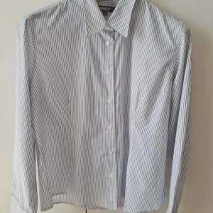 Randig skjorta från Hejco - Säljer en stilren randig skjorta från Hejco i storlek 50, helt ny och oanvänd. Skjortan är vit med tunna blå ränder och har långa ärmar samt knappar framtill. Tillverkad i en blandning av bomull och polyester för en bekväm passform. Liten i storlek, passar mer till storlek 46-48. Kan hämtas i Vallentuna.