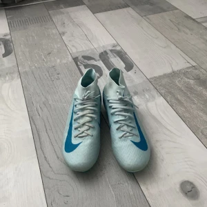 Nike Mercurial fotbollsskor i ljusblått - Säljer ett par Nike Mercurial fotbollsskor i ljusblått med blå detaljer och snörning. Skorna har en högre krage för bättre stöd och är designade för spela på konstgräs samt vanligt gräs. Skorna är helt nya använt typ 5 gånger men väljer att sälja dem då jag fått nya.