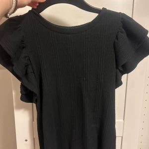 Svart ribbad tröja från zara - Svart ribbad tröja från Zara med korta volangärmar. Enkel och stilren design som passar perfekt till många tillfällen. Mjuk och stretchig känsla i materialet för extra komfort.