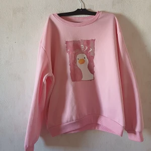 Rosa sweatshirt med anka-tryck - Säljer en söt rosa sweatshirt med ett roligt anka-tryck på framsidan. Tröjan har långa ärmar och en bekväm passform. Perfekt för en avslappnad stil!