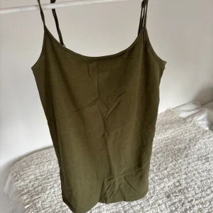 Olivgrönt linne - Säljer en stilren olivgrön linnetopp med smala axelband. Perfekt för varma sommardagar eller som ett lager under en tröja. Enkel och mångsidig design. Säljer då den inte kommer till användning😊